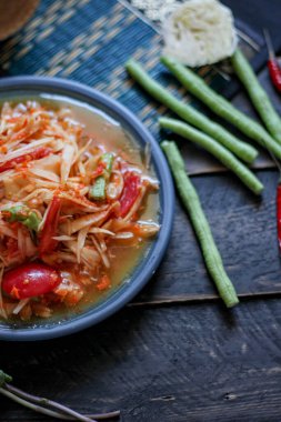 Baharatlı papaya salatası mavi bir tabakta, kovada pilav ve uzun fasulye, kurutulmuş kırmızı biber ve sebze ile servis edilir..