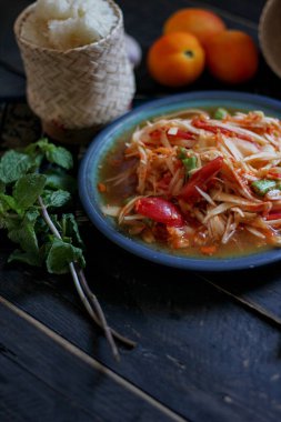 Baharatlı papaya salatası mavi bir tabakta, kovada pilav ve uzun fasulye, kurutulmuş kırmızı biber ve sebze ile servis edilir..
