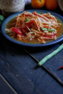 Baharatlı papaya salatası mavi bir tabakta, kovada pilav ve uzun fasulye, kurutulmuş kırmızı biber ve sebze ile servis edilir..
