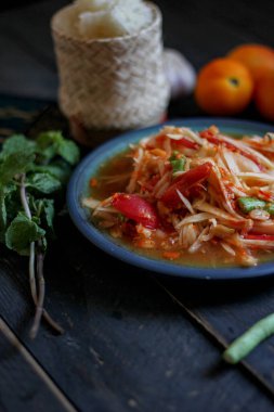 Baharatlı papaya salatası mavi bir tabakta, kovada pilav ve uzun fasulye, kurutulmuş kırmızı biber ve sebze ile servis edilir..