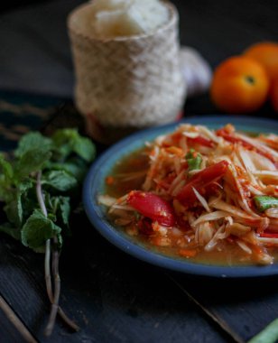 Baharatlı papaya salatası mavi bir tabakta, kovada pilav ve uzun fasulye, kurutulmuş kırmızı biber ve sebze ile servis edilir..