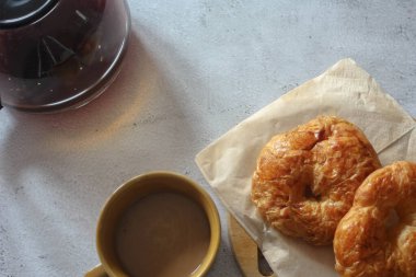 Kahveyle servis edilen bir kruvasan beyaz bir masaya konur..