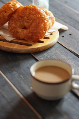 Kruvasan, siyah ahşap bir masada kahve ile servis edilir..