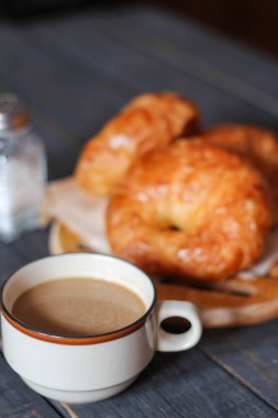 Kruvasan, siyah ahşap bir masada kahve ile servis edilir..