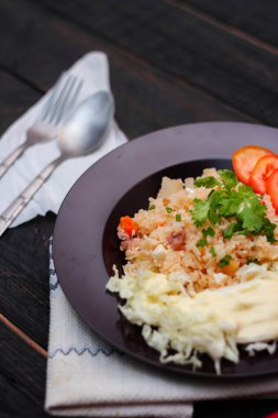 Dilimlenmiş domatesli ve siyah ahşap masada servis edilen sebze salatalı siyah tabakta kızarmış yumurta pilavı..