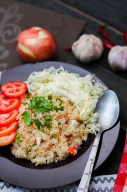 Dilimlenmiş domatesli ve siyah ahşap masada servis edilen sebze salatalı siyah tabakta kızarmış yumurta pilavı..