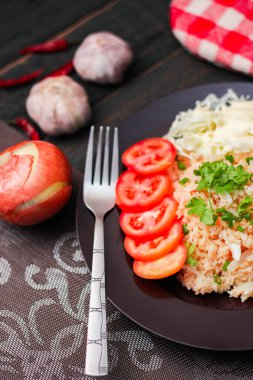 Dilimlenmiş domatesli ve siyah ahşap masada servis edilen sebze salatalı siyah tabakta kızarmış yumurta pilavı..