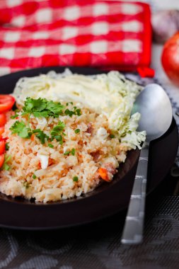 Dilimlenmiş domatesli ve siyah ahşap masada servis edilen sebze salatalı siyah tabakta kızarmış yumurta pilavı..