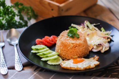 Kızarmış pirinç, sahanda yumurta, salatalık, dilimlenmiş domates, yeşil salata ve garnitür olarak siyah tabağa konmuş kızarmış tavuk.