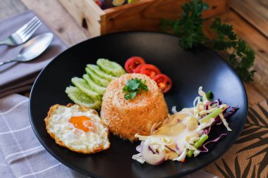 Kızarmış pirinç, sahanda yumurta, salatalık, dilimlenmiş domates, yeşil salata ve garnitür olarak siyah tabağa konmuş kızarmış tavuk.