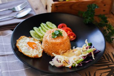 Kızarmış pirinç, sahanda yumurta, salatalık, dilimlenmiş domates, yeşil salata ve garnitür olarak siyah tabağa konmuş kızarmış tavuk.