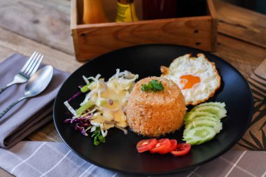 Kızarmış pirinç, sahanda yumurta, salatalık, dilimlenmiş domates, yeşil salata ve garnitür olarak siyah tabağa konmuş kızarmış tavuk.