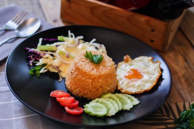 Kızarmış pirinç, sahanda yumurta, salatalık, dilimlenmiş domates, yeşil salata ve garnitür olarak siyah tabağa konmuş kızarmış tavuk.