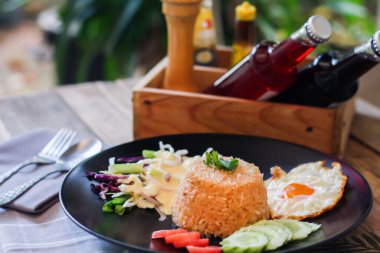 Kızarmış pirinç, sahanda yumurta, salatalık, dilimlenmiş domates, yeşil salata ve garnitür olarak siyah tabağa konmuş kızarmış tavuk.