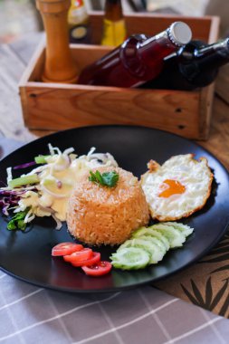 Kızarmış pirinç, sahanda yumurta, salatalık, dilimlenmiş domates, yeşil salata ve garnitür olarak siyah tabağa konmuş kızarmış tavuk.