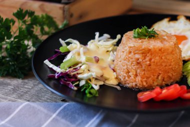 Kızarmış pirinç, sahanda yumurta, salatalık, dilimlenmiş domates, yeşil salata ve garnitür olarak siyah tabağa konmuş kızarmış tavuk.