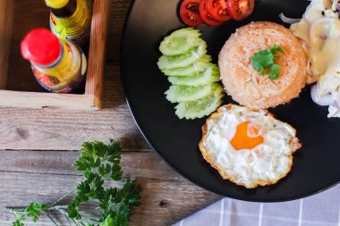 Kızarmış pirinç, sahanda yumurta, salatalık, dilimlenmiş domates, yeşil salata ve garnitür olarak siyah tabağa konmuş kızarmış tavuk.