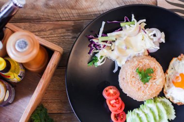 Kızarmış pirinç, sahanda yumurta, salatalık, dilimlenmiş domates, yeşil salata ve garnitür olarak siyah tabağa konmuş kızarmış tavuk.