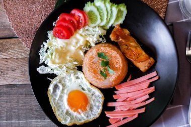 Kızarmış pirinç, sahanda yumurta, salatalık, dilimlenmiş domates, yeşil salata ve garnitür olarak siyah tabağa konmuş kızarmış tavuk..