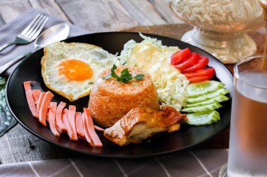 Kızarmış pirinç, sahanda yumurta, salatalık, dilimlenmiş domates, yeşil salata ve garnitür olarak siyah tabağa konmuş kızarmış tavuk..