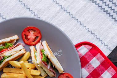 Kulüp sandviç, dört dilim domates ve patates kızartması ile gri bir tabağa serilmiş.