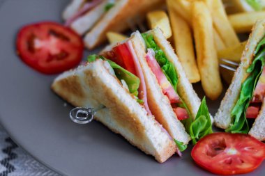 Kulüp sandviç, dört dilim domates ve patates kızartması ile gri bir tabağa serilmiş.