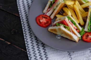 Kulüp sandviç, dört dilim domates ve patates kızartması ile gri bir tabağa serilmiş.