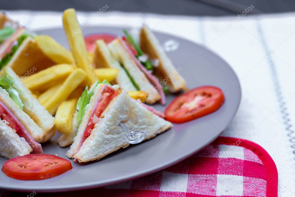 Club sandwich, 4 slices laid out on a gray plate with tomatoes and fries