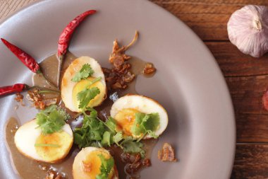 Tahta bir masada kişniş parçacıkları ile servis edilen Tamarind soslu yumurta Taylandlıların yediği popüler bir yerel yemektir..