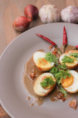 Tahta bir masada kişniş parçacıkları ile servis edilen Tamarind soslu yumurta Taylandlıların yediği popüler bir yerel yemektir..