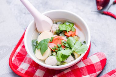 Beyaz bardaklarda servis edilen haşlanmış tofu ve kıymalı domuz eti ile beyaz masaya yerleştirilmiş kırmızı kareli çay tabakları..