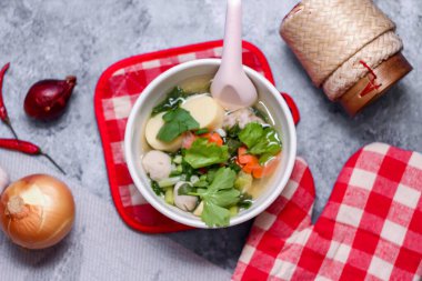 Beyaz bardaklarda servis edilen haşlanmış tofu ve kıymalı domuz eti ile beyaz masaya yerleştirilmiş kırmızı kareli çay tabakları..