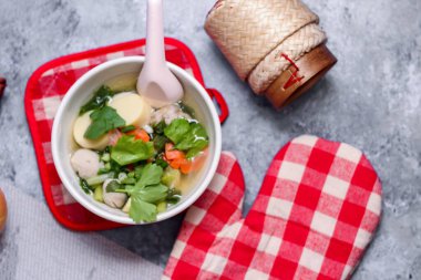 Beyaz bardaklarda servis edilen haşlanmış tofu ve kıymalı domuz eti ile beyaz masaya yerleştirilmiş kırmızı kareli çay tabakları..