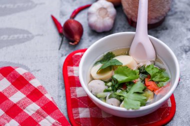 Beyaz bardaklarda servis edilen haşlanmış tofu ve kıymalı domuz eti ile beyaz masaya yerleştirilmiş kırmızı kareli çay tabakları..