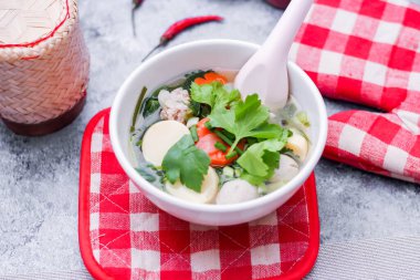 Beyaz bardaklarda servis edilen haşlanmış tofu ve kıymalı domuz eti ile beyaz masaya yerleştirilmiş kırmızı kareli çay tabakları..