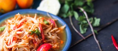 Baharatlı papaya salatası mavi bir tabakta, kovada pilav ve uzun fasulye, kurutulmuş kırmızı biber ve sebze ile servis edilir..