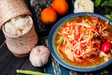 Baharatlı papaya salatası mavi bir tabakta, kovada pilav ve uzun fasulye, kurutulmuş kırmızı biber ve sebze ile servis edilir..