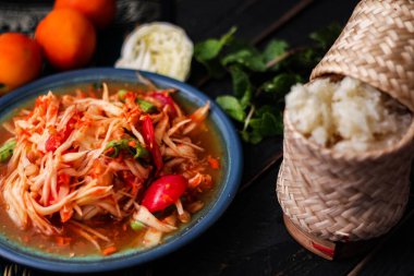 Baharatlı papaya salatası mavi bir tabakta, kovada pilav ve uzun fasulye, kurutulmuş kırmızı biber ve sebze ile servis edilir..