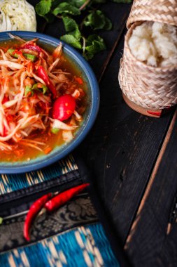 Baharatlı papaya salatası mavi bir tabakta, kovada pilav ve uzun fasulye, kurutulmuş kırmızı biber ve sebze ile servis edilir..