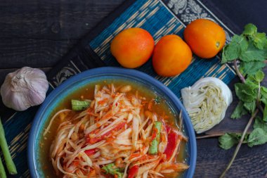 Baharatlı papaya salatası mavi bir tabakta, kovada pilav ve uzun fasulye, kurutulmuş kırmızı biber ve sebze ile servis edilir..