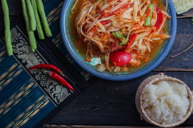 Baharatlı papaya salatası mavi bir tabakta, kovada pilav ve uzun fasulye, kurutulmuş kırmızı biber ve sebze ile servis edilir..