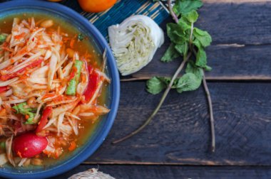 Baharatlı papaya salatası mavi bir tabakta, kovada pilav ve uzun fasulye, kurutulmuş kırmızı biber ve sebze ile servis edilir..