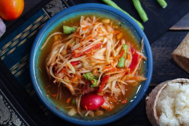 Baharatlı papaya salatası mavi bir tabakta, kovada pilav ve uzun fasulye, kurutulmuş kırmızı biber ve sebze ile servis edilir..