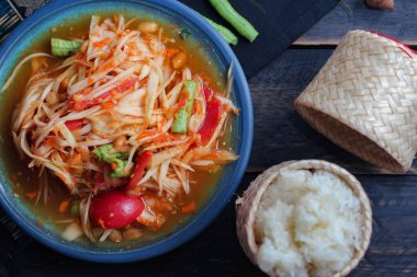 Baharatlı papaya salatası mavi bir tabakta, kovada pilav ve uzun fasulye, kurutulmuş kırmızı biber ve sebze ile servis edilir..