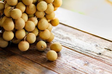 Bir grup Longan, arkasında yeşil yapraklar olan ahşap bir masaya yerleştiriliyor..