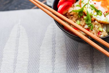 Japon usulü kızarmış pirinç, kızarmış yumurta ve kırmızı domates dilimleriyle birlikte siyah bir kasede servis ediliyor..