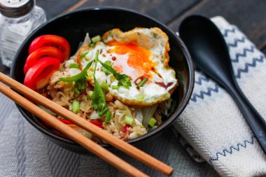 Japon usulü kızarmış pirinç, kızarmış yumurta ve kırmızı domates dilimleriyle birlikte siyah bir kasede servis ediliyor..