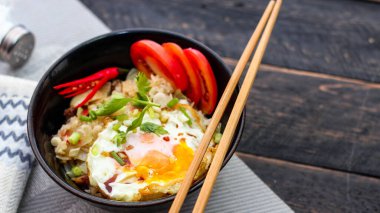 Japon usulü kızarmış pirinç, kızarmış yumurta ve kırmızı domates dilimleriyle birlikte siyah bir kasede servis ediliyor..