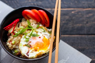 Japon usulü kızarmış pirinç, kızarmış yumurta ve kırmızı domates dilimleriyle birlikte siyah bir kasede servis ediliyor..