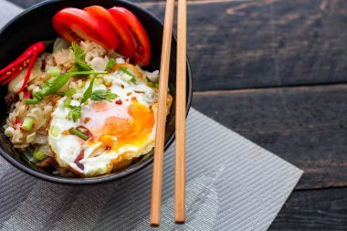 Japon usulü kızarmış pirinç, kızarmış yumurta ve kırmızı domates dilimleriyle birlikte siyah bir kasede servis ediliyor..